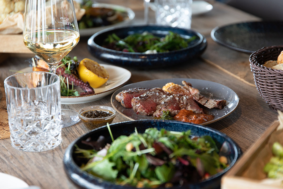 Leckere Fleisch, Fisch und Salat Gerichte serviert auf Tellern und ein Glas Weißwein in der Kutter Kitchen im arborea Marina Resort Neustadt.