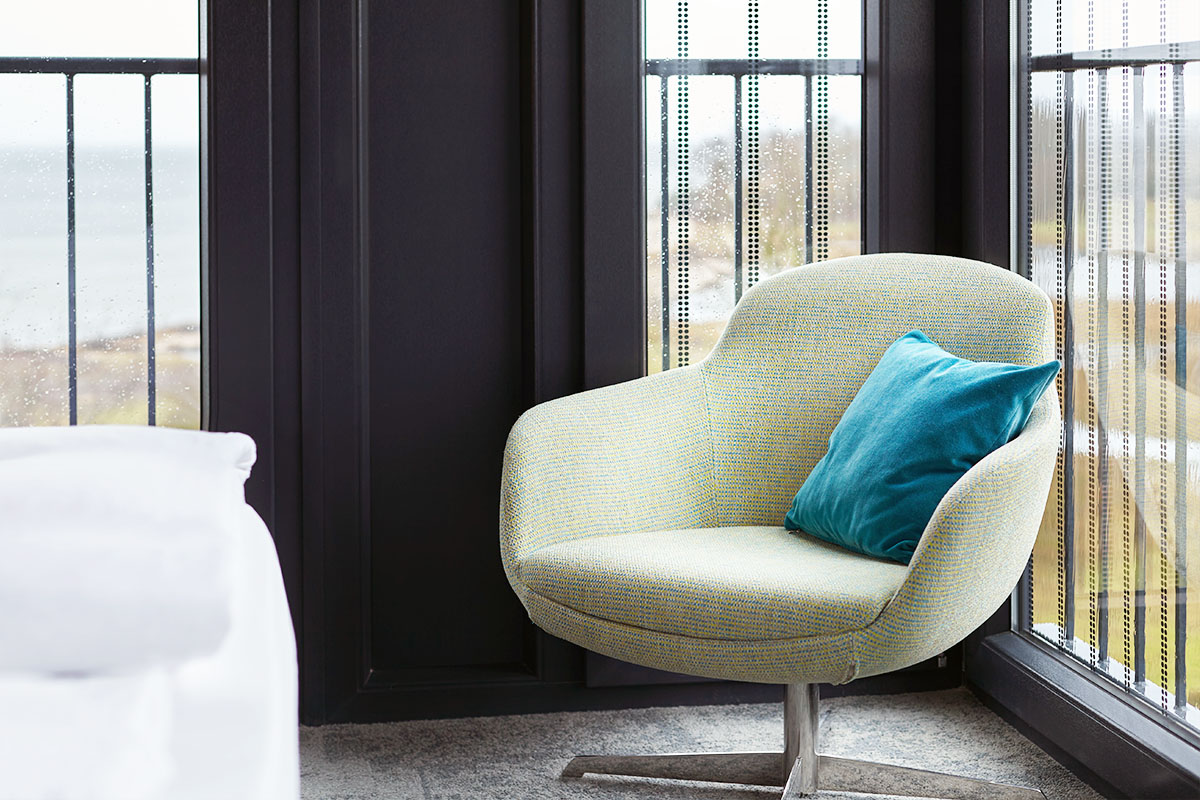Komfortabler Sessel mit einem blauen Kissen, in der Ecke des Doppelzimmers im arborea Marina Resort Neustadt.