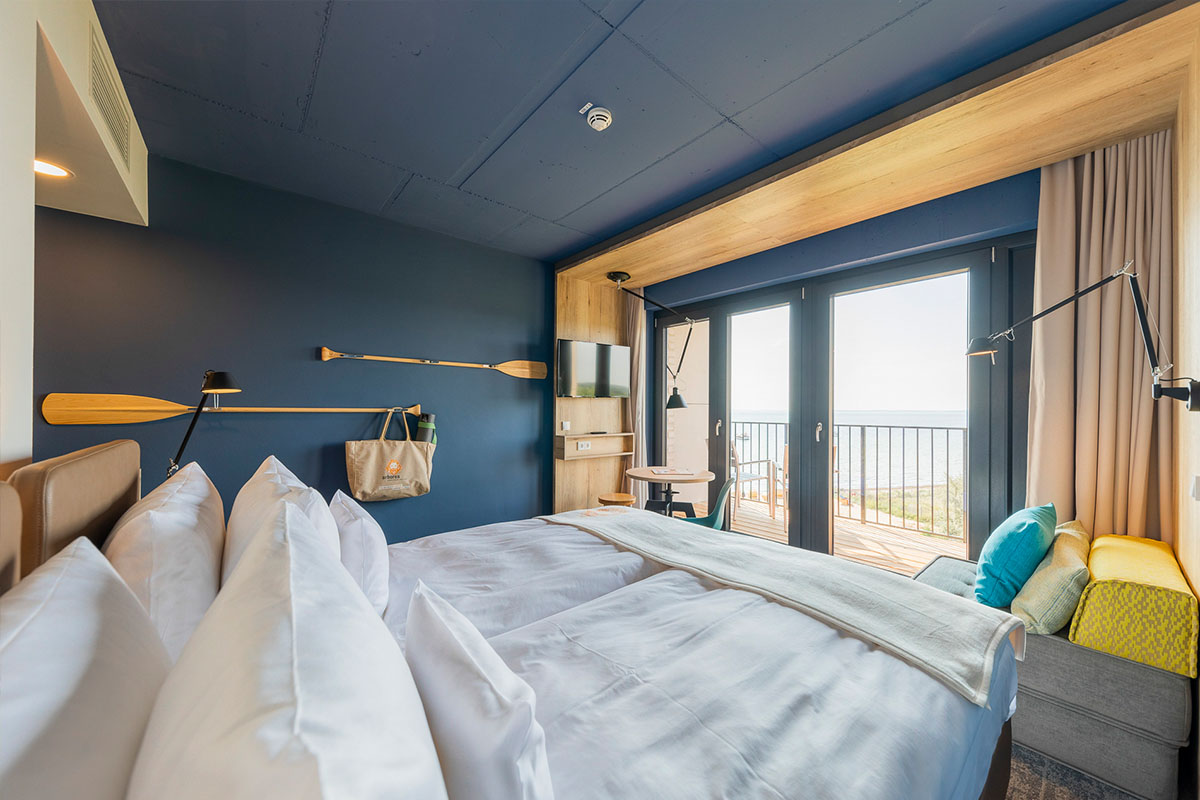 Ein Doppelzimmer im maritimen Stil mit Doppelbett und Balkon mit Blick auf die Ostsee im arborea Marina Resort Neustadt in der Lübecker Bucht.