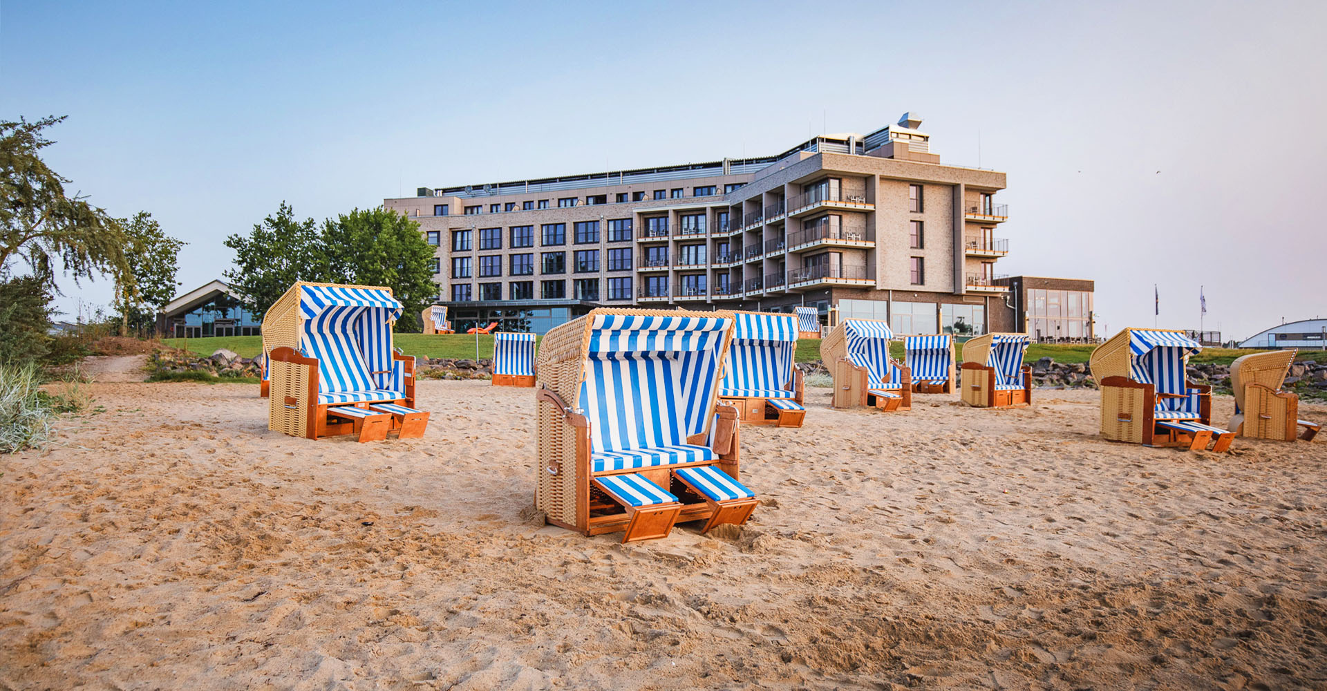 Blau und weiß gestreifte Strandkörbe am Ostseestrand vor der Außenfassade des arborea Marina Resort Neustadt.