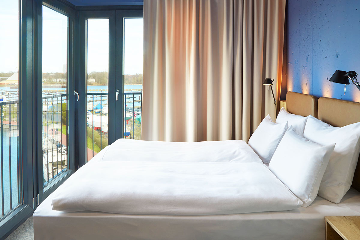 Ein gemütliches Doppelbett mit Blick auf das Meer in der ancora Suite im arborea Marina Resort Neustadt.