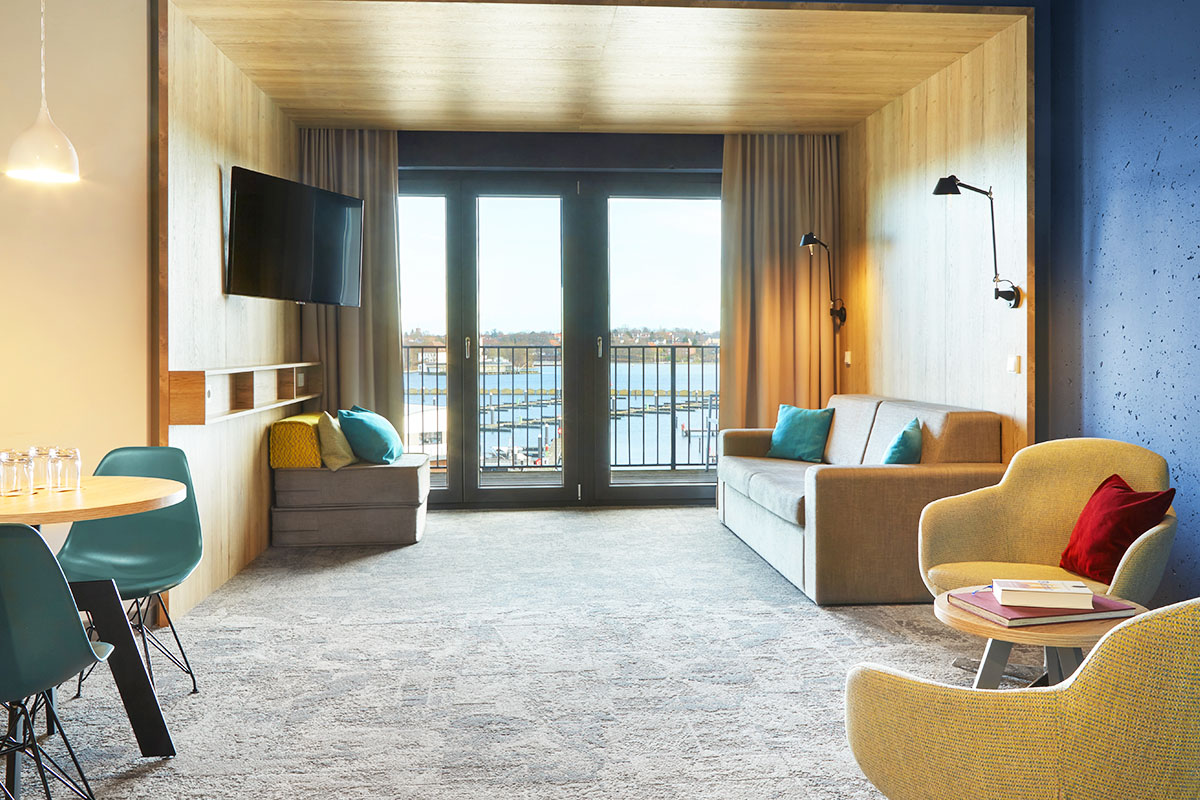 Der Wohnbereich in der ancora Suite im arborea Marina Resort Neustadt mit Sofa, Sesseln, TV, kleinem Essbereich und Balkon mit Blick auf die Ostsee.