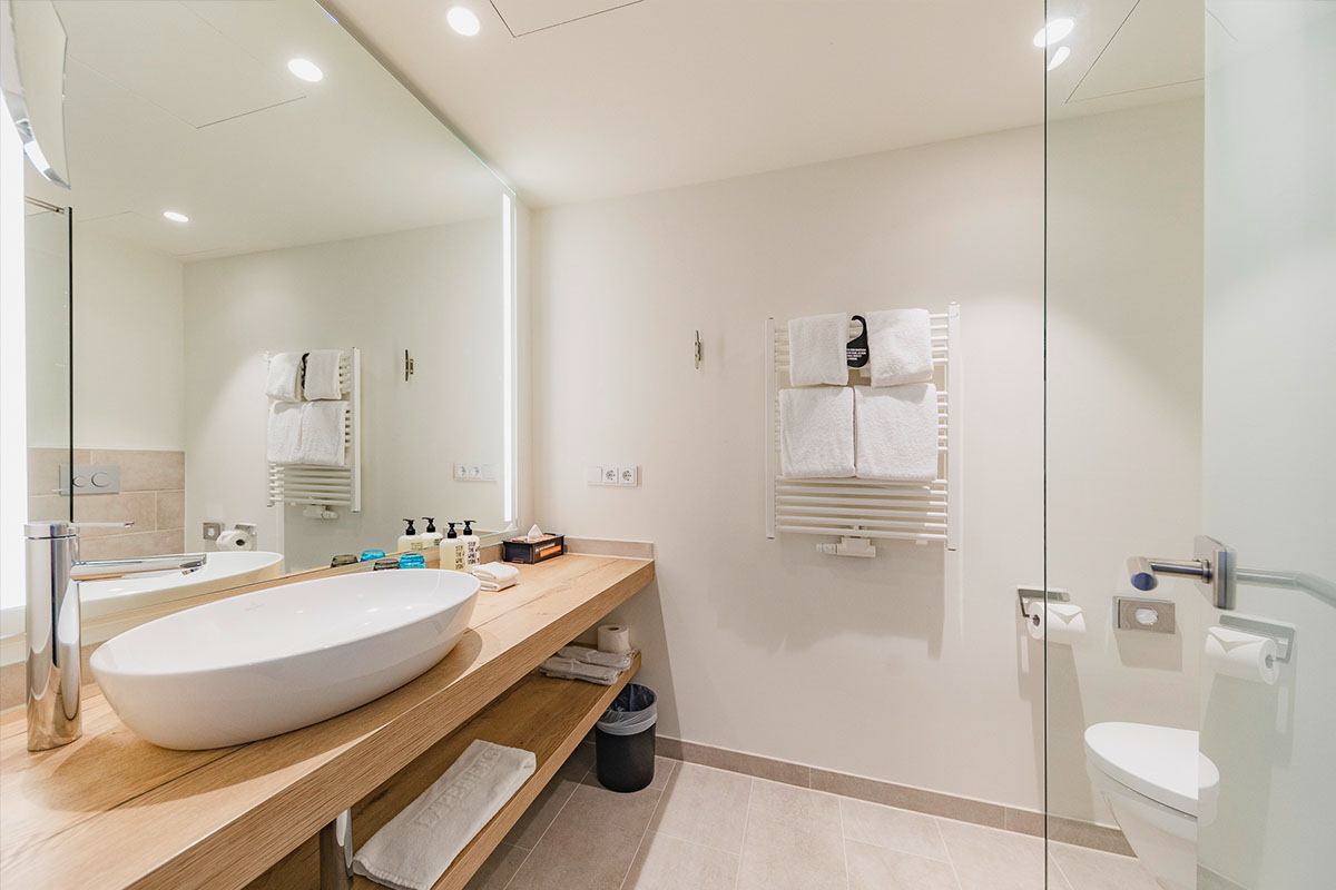 Badezimmer mit Kosmetikspiegel, Dusche, Waschbecken und Toilette inklusive Körperpflegeprodukte von RITUALS im arborea Marina Resort Neustadt.
