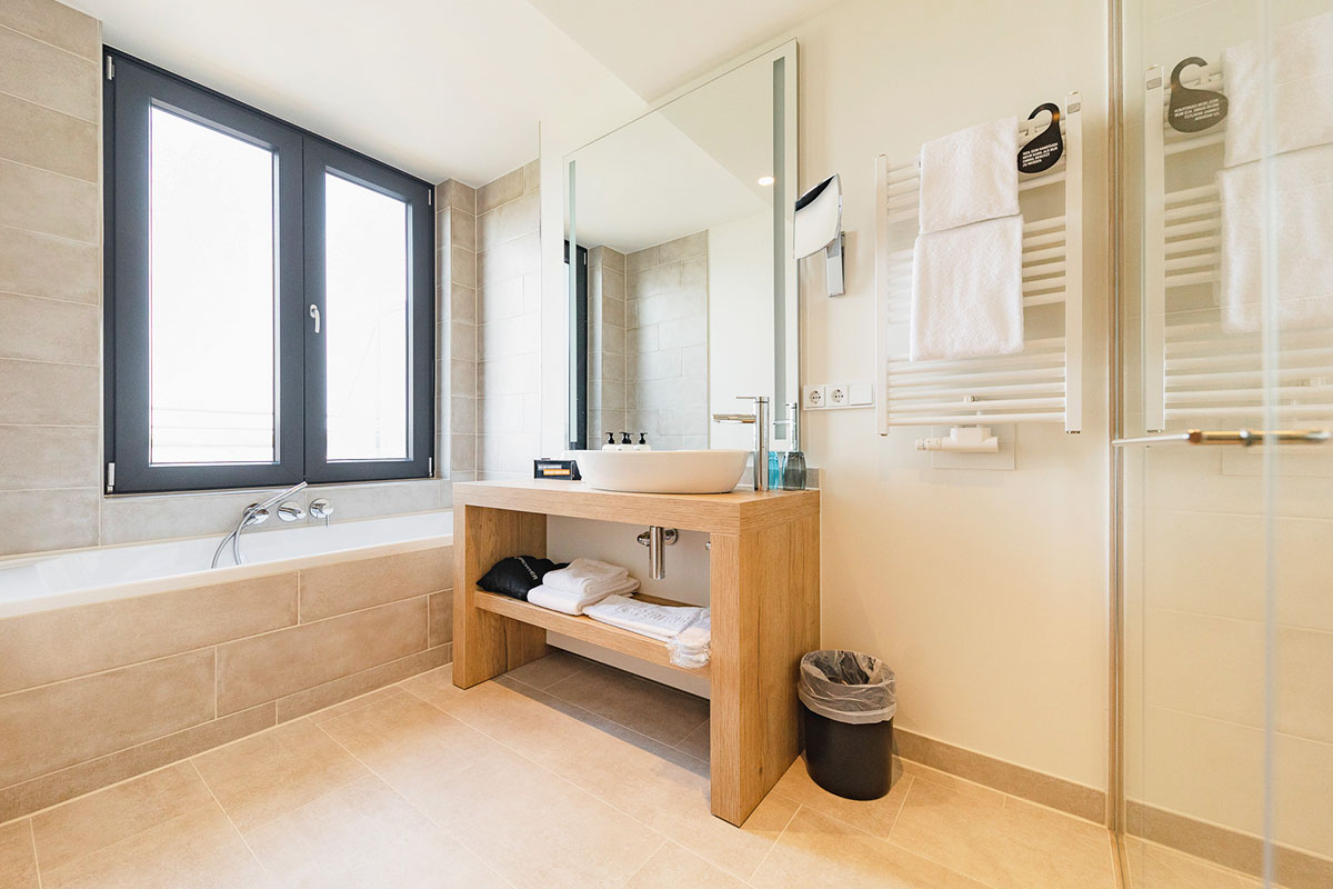 Badezimmer mit Kosmetikspiegel, Badewanne, Waschbecken und Handtücher im arborea Marina Resort Neustadt.
