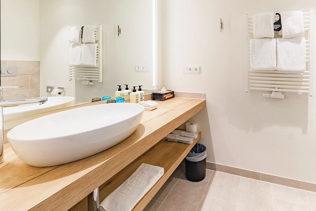 Badezimmer mit Kosmetikspiegel und Waschbecken inklusive Körperpflegeprodukte von RITUALS und Handtüchern im arborea Marina Resort Neustadt.