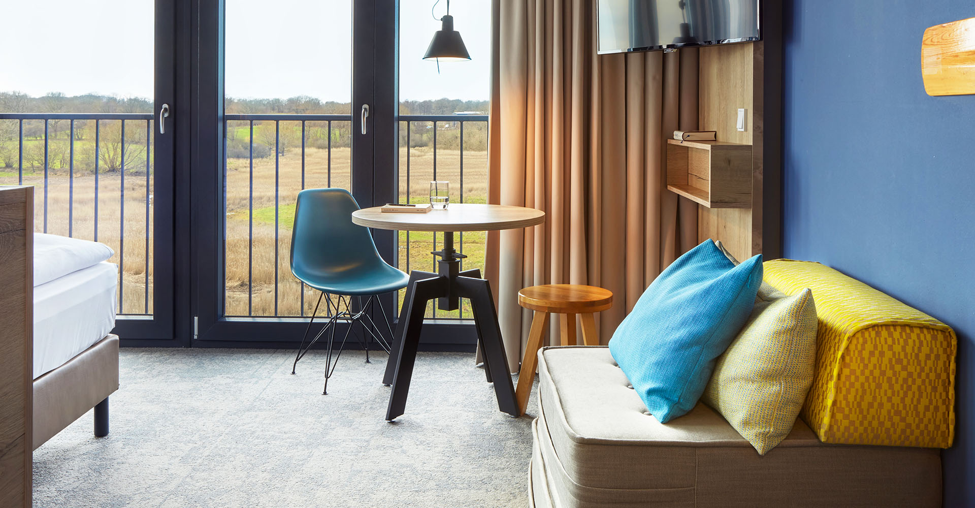 Der Wohnbereich im Doppelzimmer Landblick mit kleinem Sessel, Esstisch mit Stühlen und einem Ausblick auf die Landseite im arborea Marina Resort Neustadt.