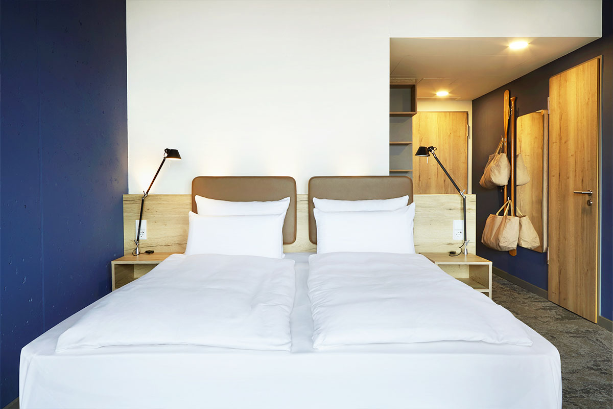 Das Kingsize Bett mit Beistelltischen im Doppelzimmer Ostsee im arborea Marina Resort Neustadt.